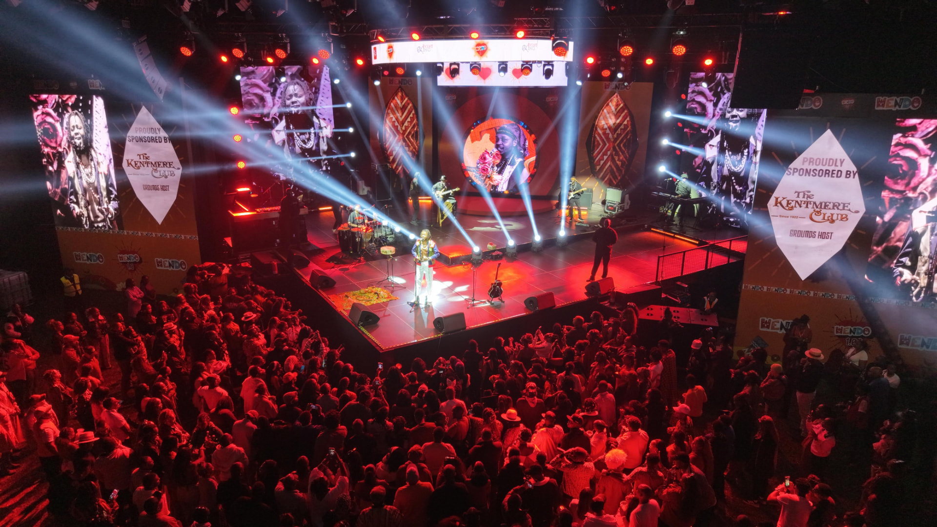 Concert performer lit by spotlights on stage before a large crowd